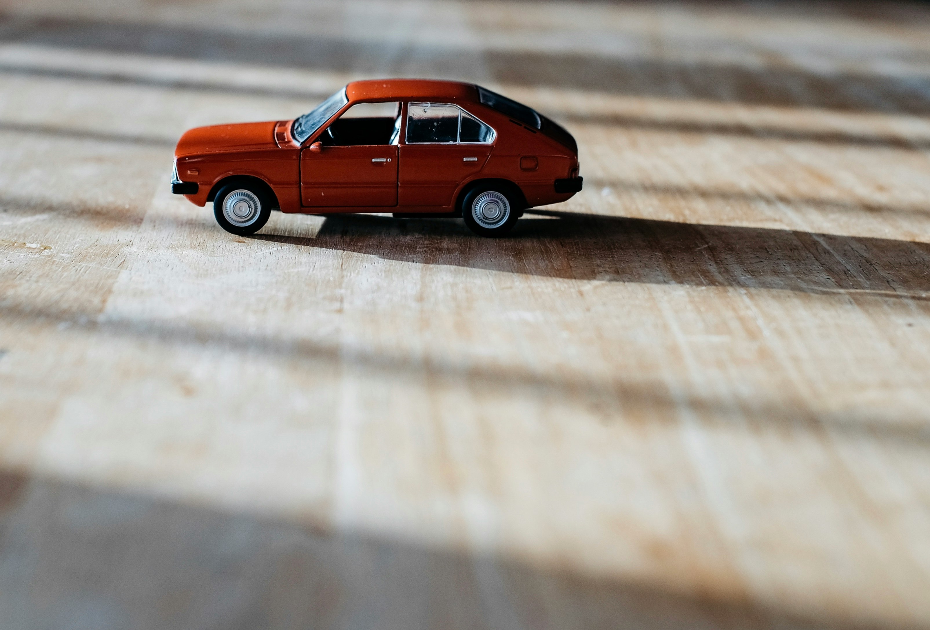 red 5-door hatchback vehicle scale model on top of brown surface